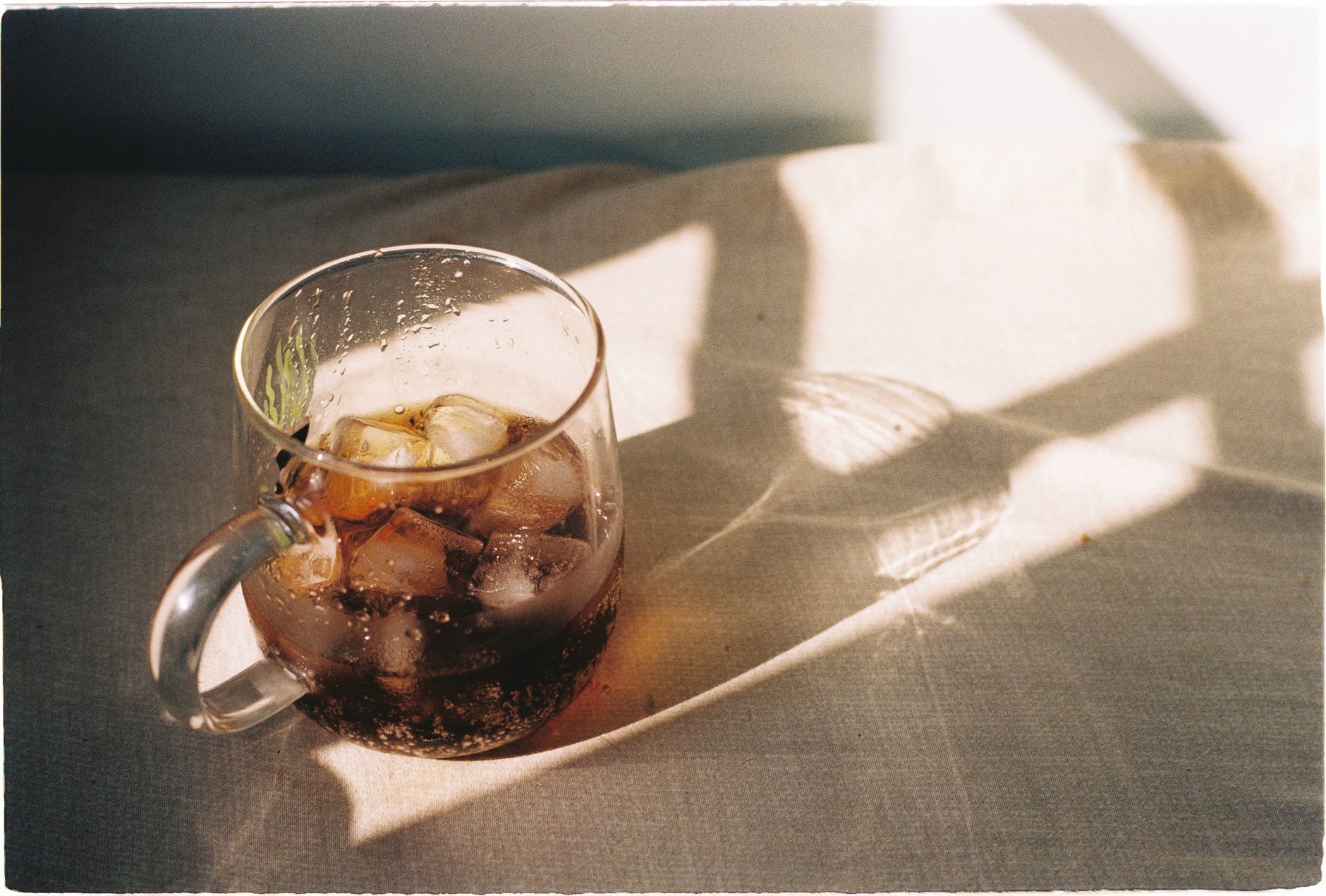 A cool glass of iced coffee catching sunlight on a bright day, perfect refreshment.