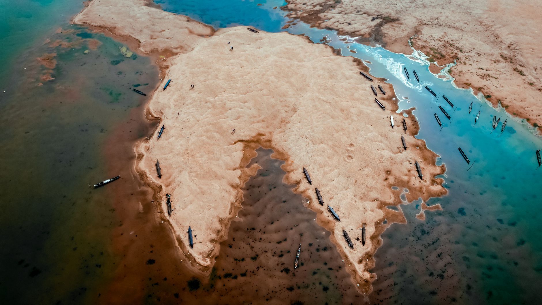 Aerial photograph showcasing a sandy island formation surrounded by clear blue water with boats scattered around.